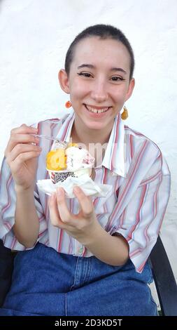 Pretty young adolescent eating a ice cream with a great smile and expression of happiness wearing a red striped white shirt with some blue jeans. Stock Photo