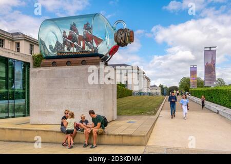 A family sit beneath Lord Nelson's Ship in a Bottle, an artwork by Yinka Shonibare, outside the National Maritime Museum in Greenwich, London. Stock Photo