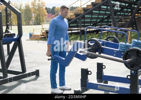 handsome man in sport outfit doing deadlift using street sport ground equipment. fit and lean man workout on a stadium in autumn season. outdoors training.  Stock Photo