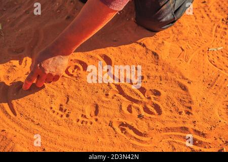 Kings Creek Station, Northern Territory, Australia - Aug 21, 2019: aboriginal woman hands creating shapes with red sand on the ground in aboriginal Stock Photo