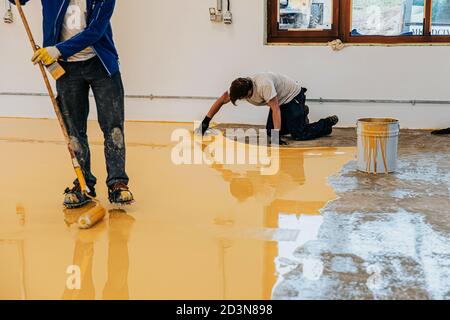 Worker, coating floor with self-leveling epoxy resin in industrial workshop. Stock Photo
