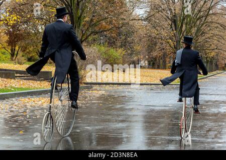 Two cyclists ride through the autumn park on Penny Farthing bicycles wearing tail coat Stock Photo