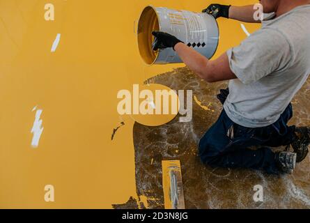 Worker, coating floor with self-leveling epoxy resin in industrial workshop. Stock Photo