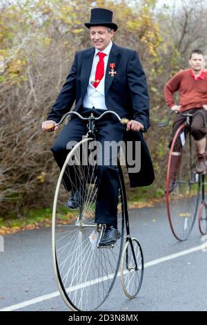 Two cyclists on Penny Farthing bicycle path wearing tail coat and top hat Stock Photo