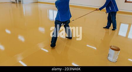 Worker, coating floor with self-leveling epoxy resin in industrial workshop. Stock Photo