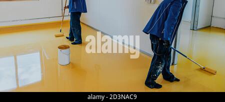 Worker, coating floor with self-leveling epoxy resin in industrial workshop. Stock Photo