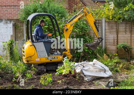 Garden clearance work and renovation taking part in garden at Bournemouth, Dorset UK in October - worker operating jcb mini excavator digger Stock Photo