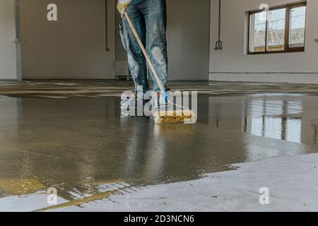 Worker, coating floor with self-leveling epoxy resin in industrial workshop. Stock Photo