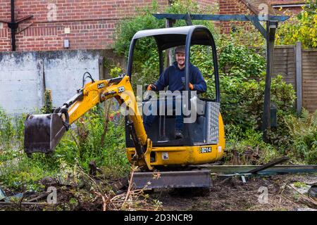 Garden clearance work and renovation taking part in garden at Bournemouth, Dorset UK in October - worker operating jcb mini excavator digger Stock Photo