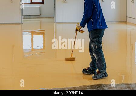 Worker, coating floor with self-leveling epoxy resin in industrial workshop. Stock Photo