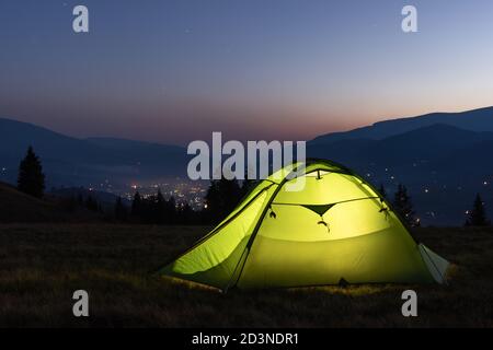 Green tent lighted from the inside by a flashlight against the backdrop of an incredible mountain landscape. Amazing evening highland. Tourism concept Stock Photo
