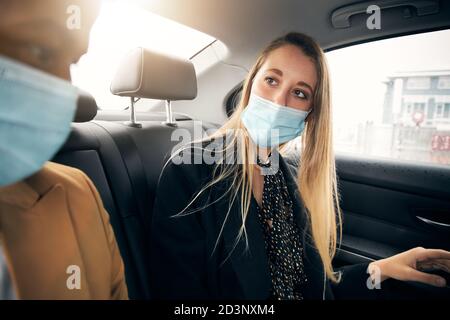 Business Couple Wearing Masks Having Conversation In Back Of Taxi During Health Pandemic Stock Photo
