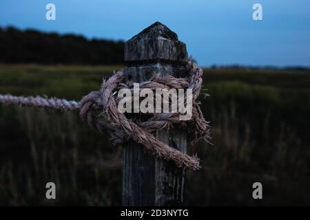 The tied rope in a knot around the wooden rode at the dusk, green grass, and night skies are in the background. Stock Photo