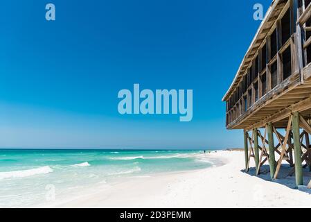 An old wooden beach house next to a clear blue ocean and white sand beach on Shell Island, Panama City, Florida