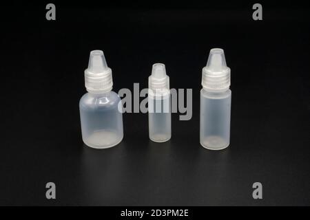 Empty, clear, transparent plastic containers. Isolated small tubes with white caps on dark background Stock Photo