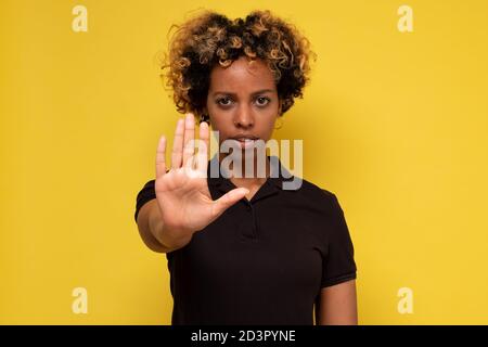 Young woman makes a gesture stop, on a yellow background Stock Photo