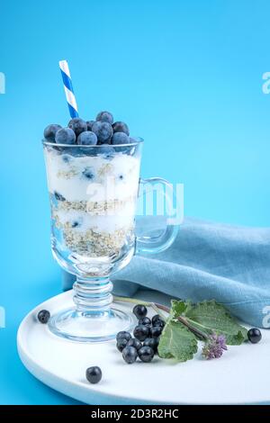 A glass with a cocktail with berries and a straw on a white plate on a blue background. Stock Photo