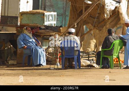 In Luxor town, the rhythm of life is calm. Three men are sitting in the corner of the market square. One is smoking a hookah. Stock Photo