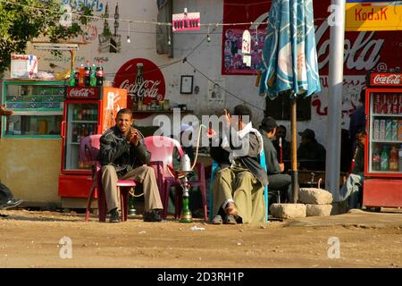 In Luxor town, the rhythm of life is calm. Two men are sitting in the corner of the market square. One is smoking a hookah. Stock Photo