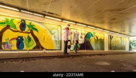Colourful wall paintings or street art in a subway or underpass in Aldershot town, Hampshire, UK with a senior couple wearing face masks