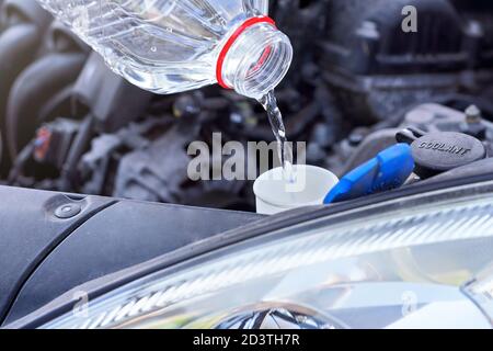 Pouring distilled water (ecological alternative to washing fluid) to washer tank in car, detail on clear plastic bottle Stock Photo