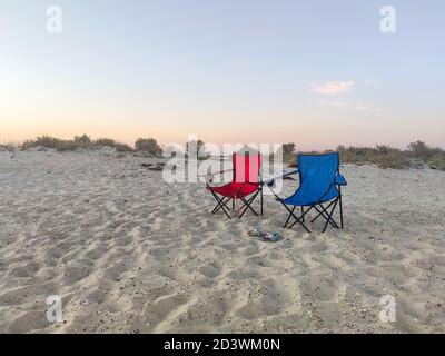 Couple of folding chairs on sandy beach in evening. Rest, camping. Stock Photo