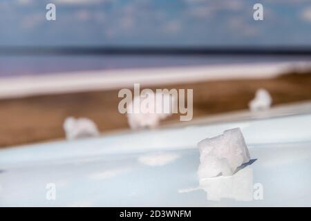 Pink white salt flake crystal formation on white reflective surface with blurred pink salty lake landscape background. Spa resort sunny close-up Stock Photo