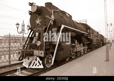 A man stands on a vintage train. The man shows forward on an old steam locomotive. Retro Union head car of the train. ?lack-white style, Lenin's gestu Stock Photo