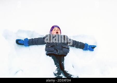 the boy is lying on the snow in the pose of a snow angel child on ice in a snow park