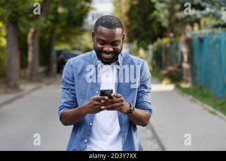Happy man using mobile phone apps, texting message, browsing internet, looking at smartphone. Handsome Afro-American man using smartphone and smiling Stock Photo