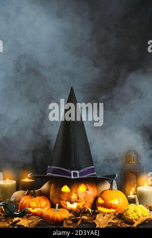 Jack o lantern with a witch hat, on a foggy background and with dry leaves, candles and some other pumpkins. Stock Photo