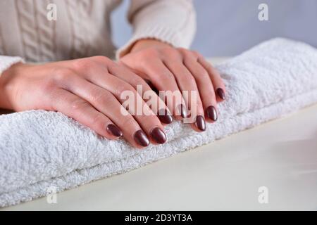 Female hands with brown nails polish color on a towel in a beauty salon on a white desk. Manicure and beauty concept Stock Photo