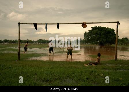 Children play football on a field, which is partly flooded and is located between two public cemetery sites in Pondok Kelapa, Jakarta, Indonesia. Stock Photo