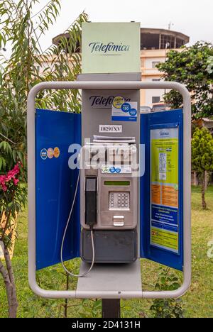 Lima, Peru - December 4, 2008: closeup of Telefonica public coin-operated telephone booth. Metal gray and blue, surrounded by green lawn and plants. S Stock Photo