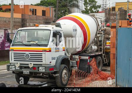 Lima, Peru - December 4, 2008: Closeup of white Volkswagen cement truck unloading at building site in neighborhood. Workers present, green foliage and Stock Photo