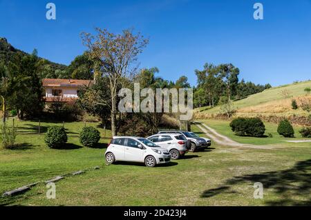 Cars parked on a green grass field outside Wolkenburg brewery located at Cunha countryside and under late afternoon blue sky. Stock Photo