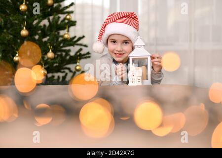 A child in a New Year's cap, lies on his palm in a hug with a lamp house and smiles broadly lips.  Stock Photo