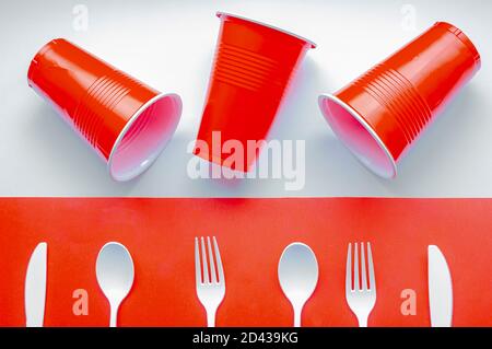 Single use white plastic cutlery and red plastic glass on a red and white background. Concept: Ban single use plastic Stock Photo