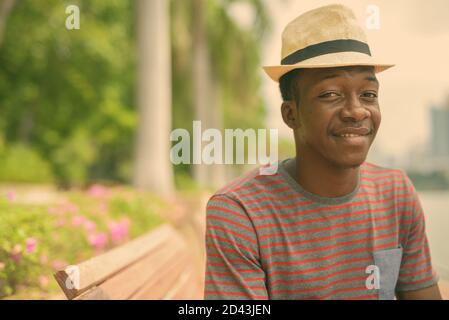 Happy young handsome African man relaxing at the park in the city Stock Photo