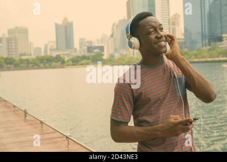 Happy young handsome African man listening to music at the park Stock Photo