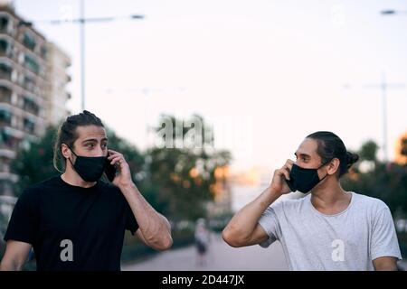 Male friends walking in the park and talking on the phone Stock Photo