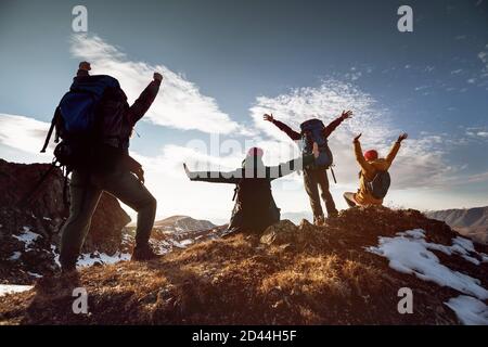 Four happy hikers stands in winner poses at mountain top at sunset time Stock Photo