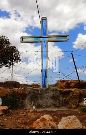 A large glass cross reflects he blue sky and clouds, surrounded by barbed wire in the grounds of the table-top mountain monastery of Debre Damo in Tig Stock Photo