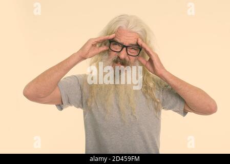 Studio shot of senior bearded man wearing eyeglasses while having headache with both hands on head Stock Photo