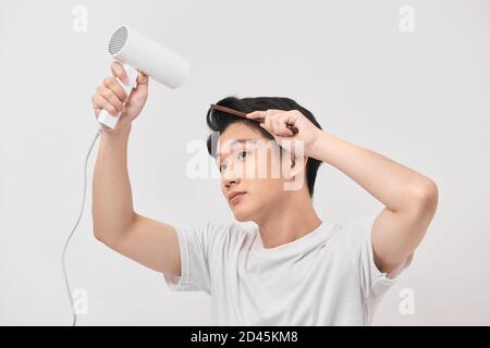 Young asian man holding hair dryer and comb creating new hairdo on white background Stock Photo