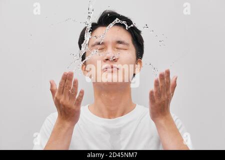 Young man spraying water on his face over gray background Stock Photo