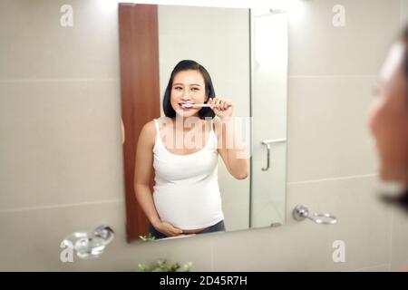 Young pregnant woman brushing teeth in bathroom Stock Photo