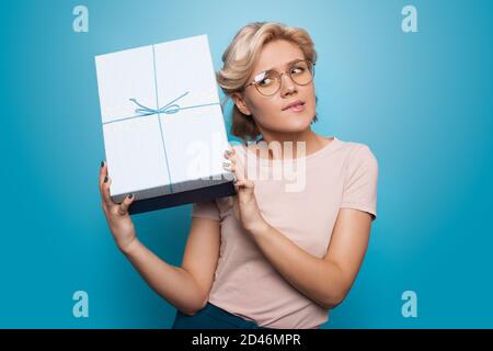 Blonde caucasian woman listening to her present gesturing impatience on a blue studio wall Stock Photo
