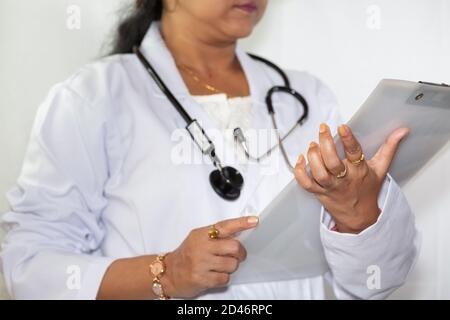 Indian female doctor wearing a stethoscope examine a medical report at a healthcare clinic Stock Photo