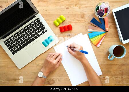 Designer workplace, top view. Home office - desk with laptop, hands with colourful set, Stock Photo